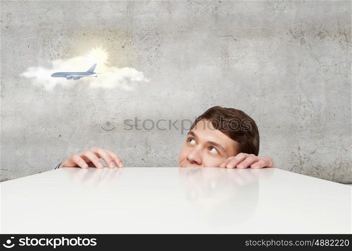 Young man looking from under table on flying airplane. No limits for communication