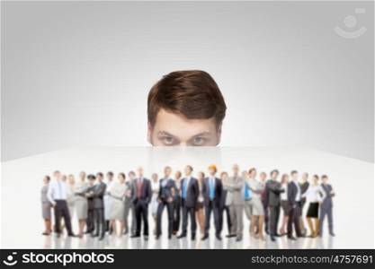 Young man looking from under table on large group of business people. They are professionals
