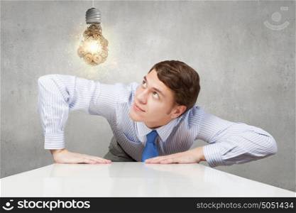 Young man looking from under table on light bulb. Business ideas