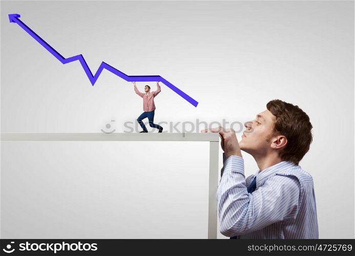 Young man looking from under table on man carrying arrow graph