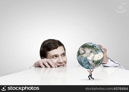 Young man looking from under table on student carrying globe. Elements of this image are furnished by NASA. Planet in our hands