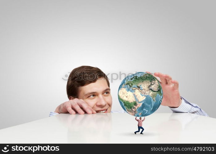 Young man looking from under table on student carrying globe. Elements of this image are furnished by NASA. Planet in our hands