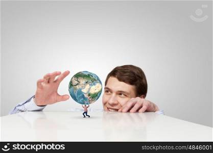 Young man looking from under table on student carrying globe. Elements of this image are furnished by NASA. Planet in our hands
