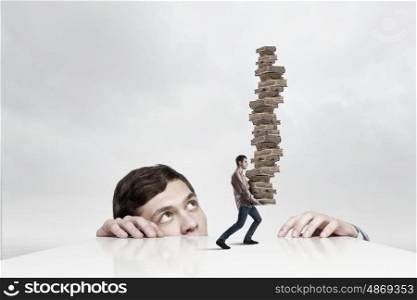 Young man looking from under table on student carrying pile of books