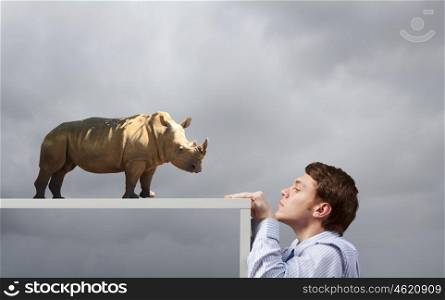 Young man looking from under table on woman fighting with massive rhino. Not on equal