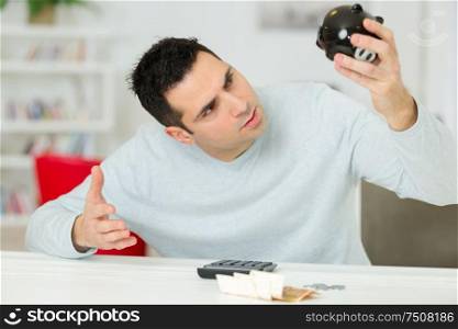 young man looking in desperation at his empty piggy bank