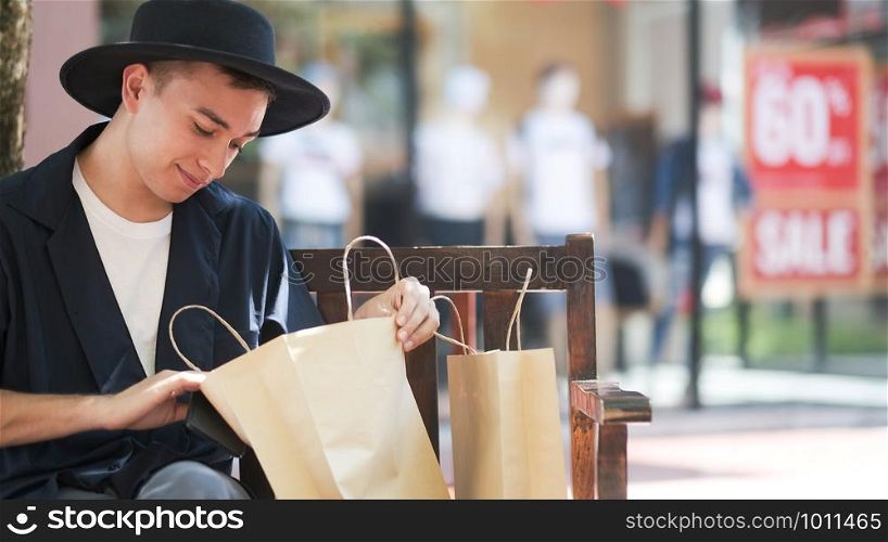 Young man looking into shopping bags. Sale, consumerism and people concept.