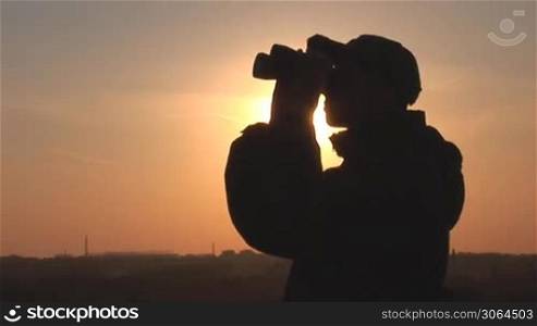 young man looking through binoculars at sunset