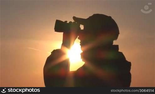 young man looking through binoculars at sunset