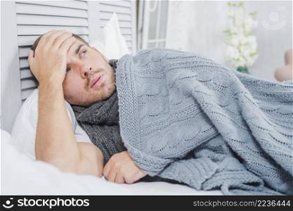 young man lying bed with headache fever touching his forehead