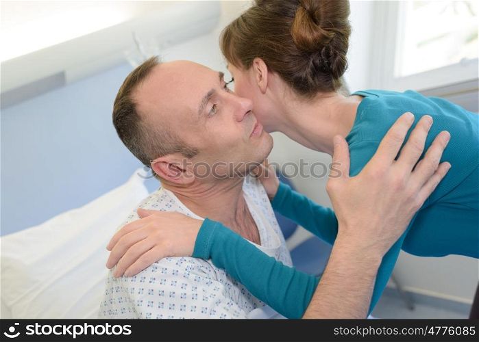 young man lying in bed at hospital and wife kissing