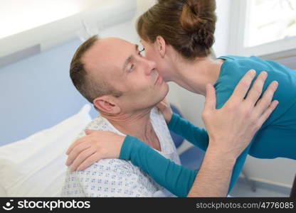 young man lying in bed at hospital and wife kissing