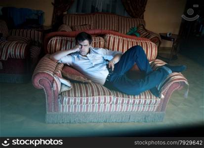 Young man lying on sofa and watching TV at night