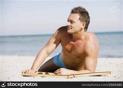 Young man lying on the beach and looking away