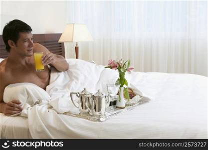 Young man lying on the bed holding a glass of orange juice