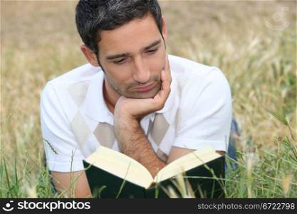 young man lying on the grass and reading a book