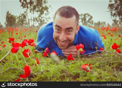 Young man lying on the grass in a field of red poppies and smiling at the camera