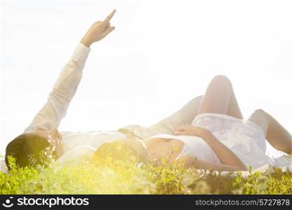 Young man lying with girlfriend while pointing against clear sky