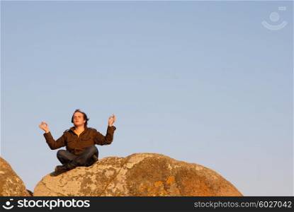 young man meditating on the rocks with the sky as background
