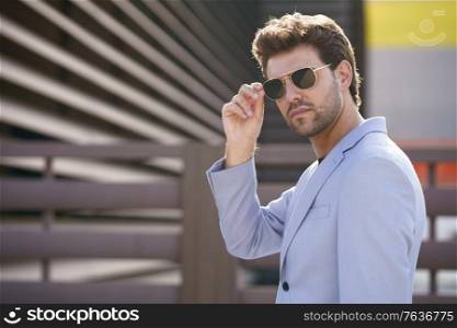 Young man, model of fashion, wearing sunglasses in urban background. Young handsome man wearing sunglasses in urban background