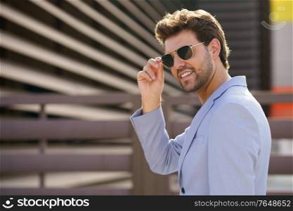 Young man, model of fashion, wearing sunglasses in urban background. Young handsome man wearing sunglasses in urban background