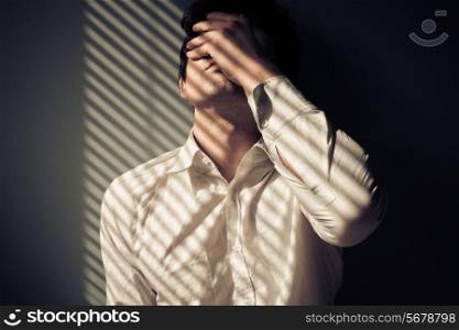 Young man next to a window with shadows being cast from the blinds
