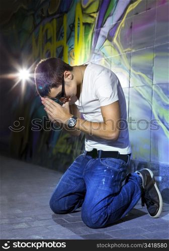 young man offers prayers in front of colorful graffiti wall
