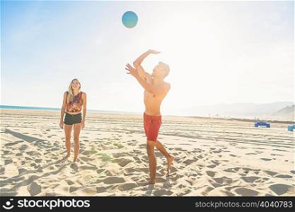 Young man on beach about to to strike volleyball