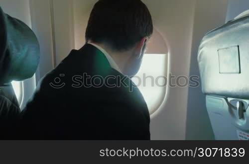 Young man on business trip. He traveling by air and using smart phone to keep in touch, sometimes looking out the illuminator