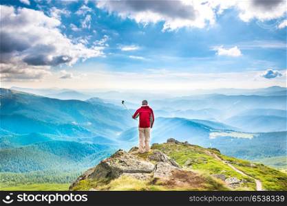 Young man on mountain taking selfie. Young man on the top of mountain taking picture with smartphone on selfie stick