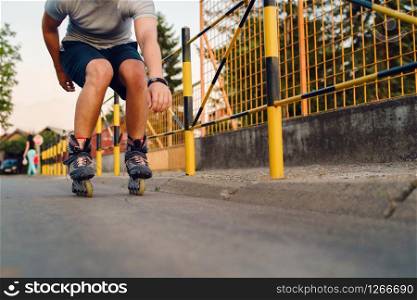 Young man on roller blades skates riding by the fence wall looking waiting in a summer day evening rollerblading on the street