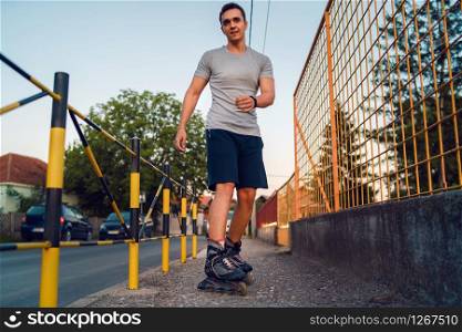 Young man on roller blades skates riding by the fence wall looking waiting in a summer day evening rollerblading