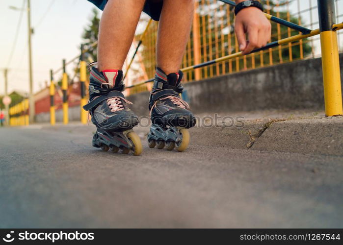 Young man on roller blades skates riding by the fence wall looking waiting in a summer day evening rollerblading on the street close up on feet