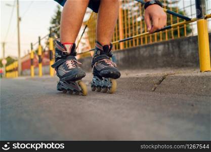 Young man on roller blades skates riding by the fence wall looking waiting in a summer day evening rollerblading on the street close up on feet
