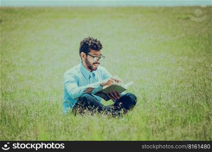 Young man on the grass reading a book, A person sitting on the grass reading a book, concept of people reading outside