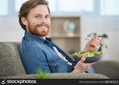 young man on the sofa eating a salad