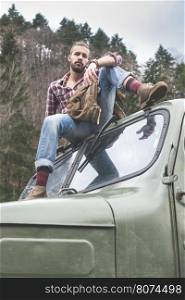 Young man on vintage truck with logs in the forest.
