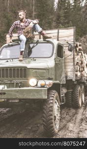 Young man on vintage truck with logs in the forest.