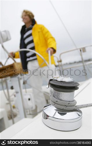 Young man on yacht in sea, focus on crank with rope