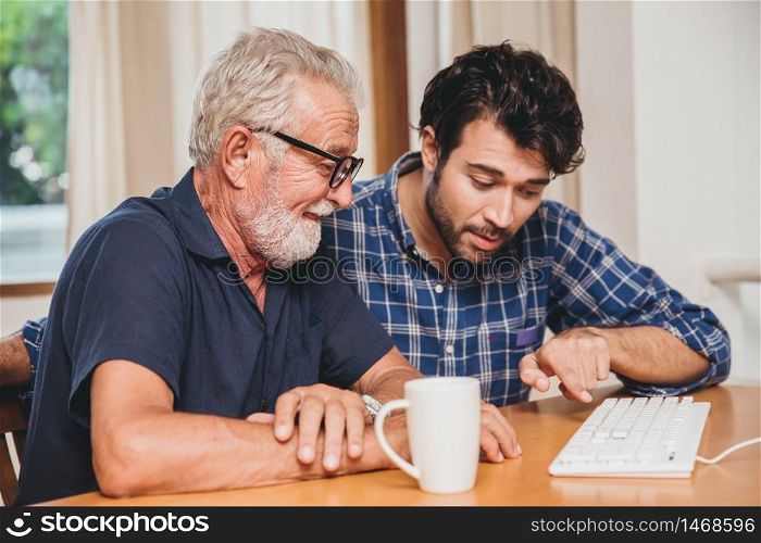 young man or son teaching his grandfather elderly dad learning to using computer at home.