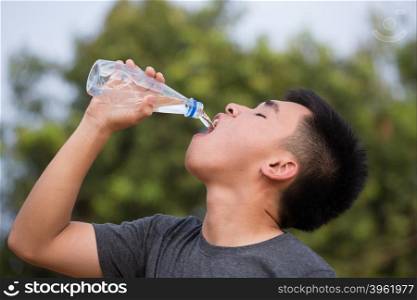 young man or teenager drinking water from plastic bottle