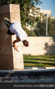 Young man performing parkour in the city. Young athlete showing skills of free running. Parkour trick with city wall