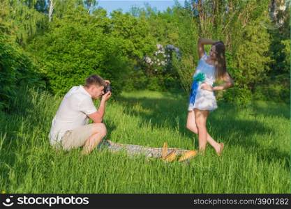Young man photographing his girlfriend at a picnic in a city park at summer day