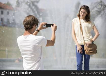 Young man photographing woman against fountain