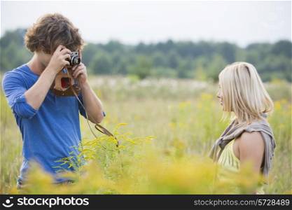 Young man photographing woman in field