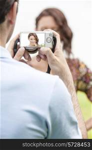 Young man photographing woman through digital camera in park