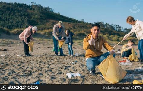 Young man picking up trash with group of volunteers on the beach. Young man cleaning the beach