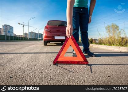 Young man placing red triangle sing on road after car crash