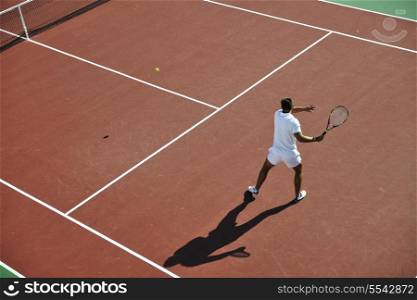 young man play tennis outdoor on orange tennis field at early morning