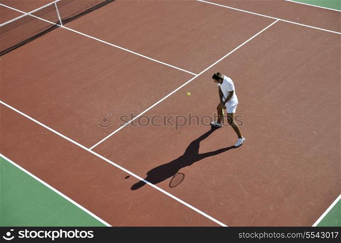 young man play tennis outdoor on orange tennis field at early morning